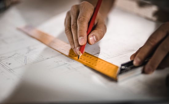 Hand holding a pencil, tracing on paper alongside a ruler